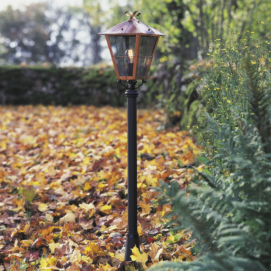 Herfsttafereel van een tuin met een zwarte paallamp met een koperkleurige kap